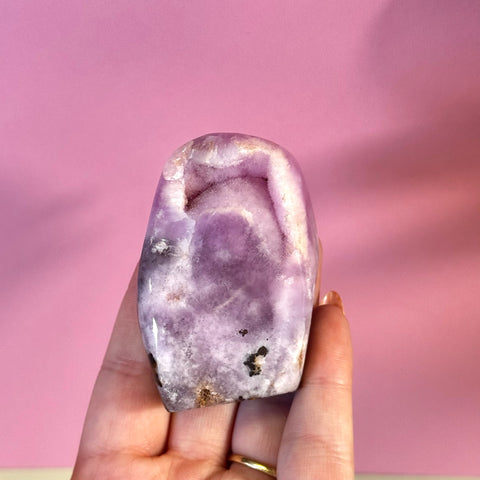 Juicy pink aragonite free form with wave-like patterning, held against a pink background.