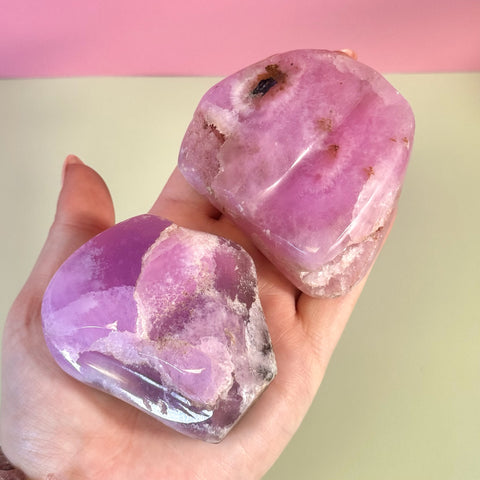 Two juicy pink aragonite free forms with wave-like patterning held in a hand.