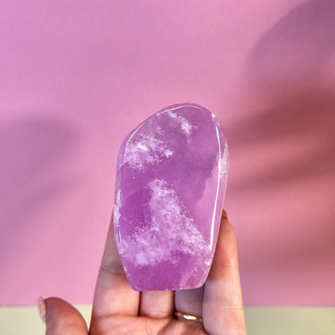 Juicy pink aragonite free form with clean, wave-like white patterning, held against a pink background.
