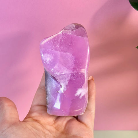 Juicy pink aragonite free form with wave-like patterning held in a hand.