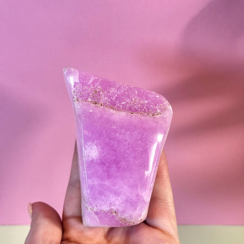 Juicy pink aragonite free form with wave-like patterning, held in a hand.