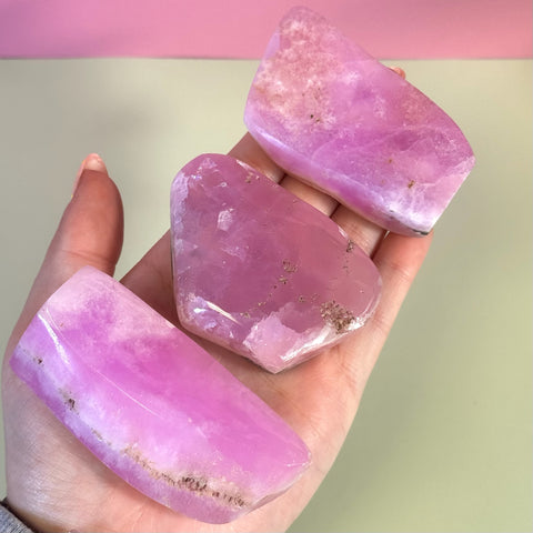 Hand holding three polished, free-form juicy pink aragonite crystals with natural variations.