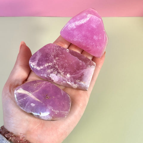 Hand holding three polished, free-form juicy pink aragonite crystals with natural white inclusions.