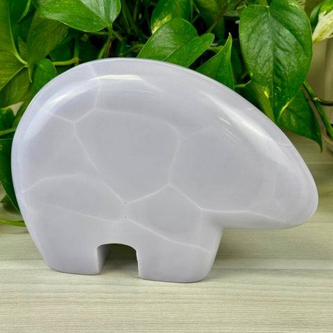 Smooth lavender fluorite bear carving with subtle white geometric patterns, against green leaves.