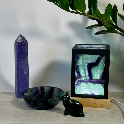 Purple fluorite tower, bowl, and cat figurine with a glowing fluorite lamp on a wooden base.