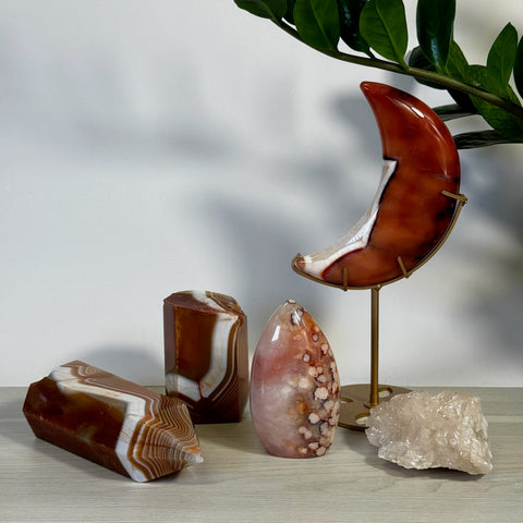 Polished red and white banded agate crystals, including a crescent moon on a stand, and a rough rose quartz chunk.