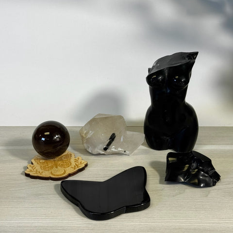 Black obsidian female torso, sphere, butterfly, and raw clear quartz crystals on a light wood surface.