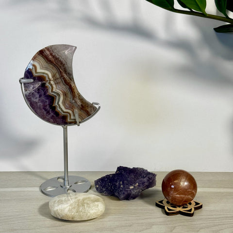 Stylized imperfect crystal bundle with a large crescent moon, raw amethyst, polished oval, and a shimmering sphere.