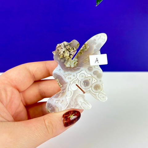 Handheld kneeling fairy princess carving made of scenic moss agate with intricate white and grey banded patterns.