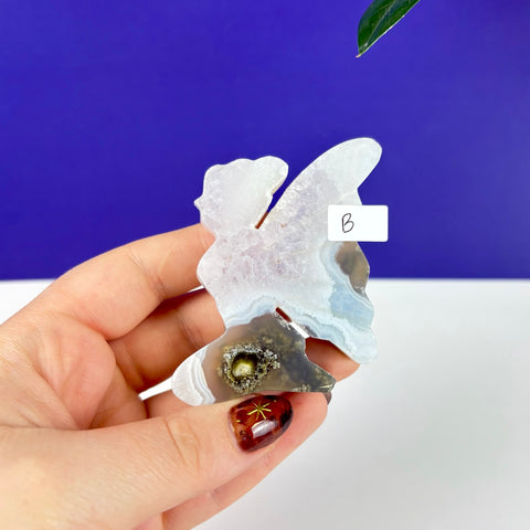 Handheld kneeling fairy carving made of translucent scenic moss agate with a unique dark druzy center.