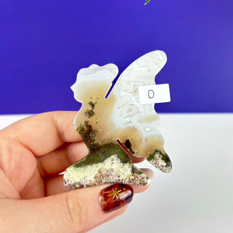 Handheld kneeling fairy figurine carved from translucent moss agate with green mineral inclusions and white banding.