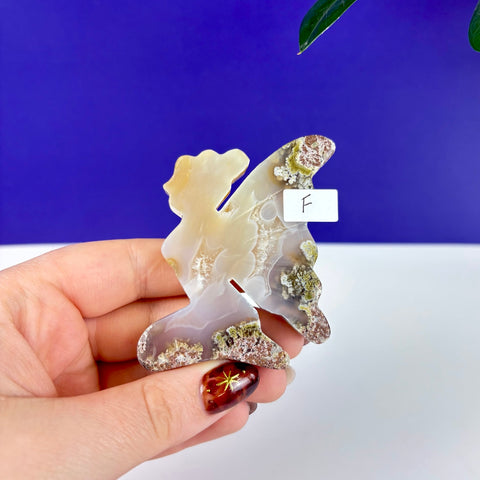 Handheld kneeling fairy carving made of translucent scenic moss agate with natural green and brown mineral inclusions.