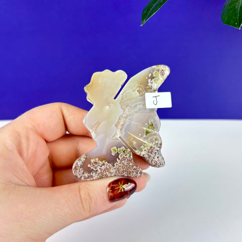 Handheld kneeling fairy figurine carved from translucent scenic moss agate with earthy green and brown mineral inclusions.