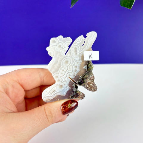 Handheld kneeling fairy princess carving made of scenic moss agate with white banded patterns and earthy mineral inclusions.