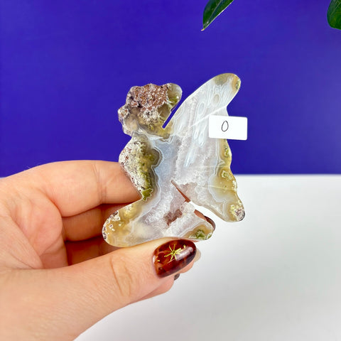 Handheld kneeling fairy princess carving made of translucent scenic moss agate with green and white mineral inclusions.