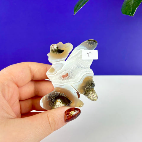 Handheld kneeling fairy princess carving made of translucent moss agate with a central druzy geode pocket.