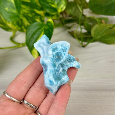 Hand holding a polished, ocean-blue Larimar freeform crystal with white wave-like patterns.