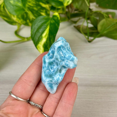 Hand holding a unique, ocean-blue Larimar freeform crystal with white wave-like patterns.
