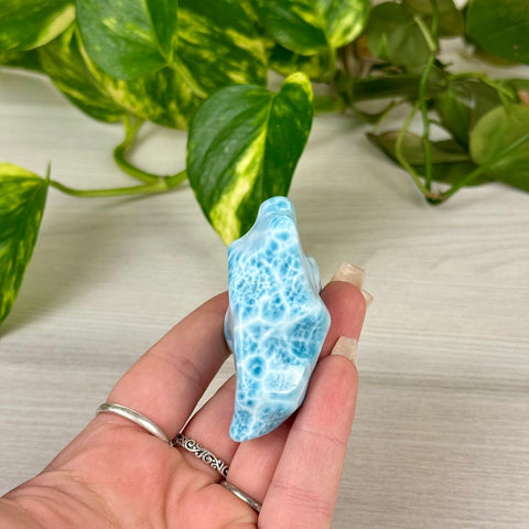 Hand holding a small, polished Larimar freeform crystal with swirling ocean-blue and white patterns.