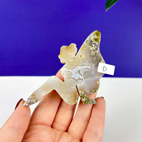 Handheld lounging fairy carving made of translucent scenic moss agate with green inclusions and white patterns.