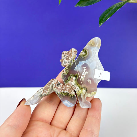 Handheld lounging fairy carving made of translucent scenic moss agate with green and brown mineral inclusions.