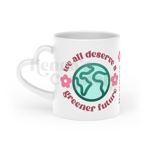 White 11oz ceramic mug with heart handle, featuring "we all deserve a greener future" text, Earth, and pink flowers.