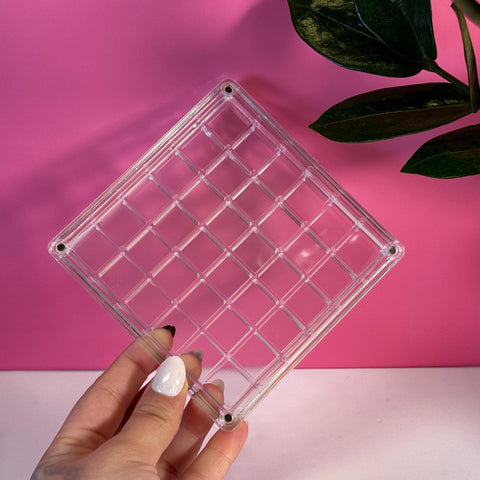 Clear acrylic mini display box with a grid design, held by a hand against a pink background.