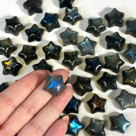 Hand holding a small, polished labradorite star with blue flash, surrounded by similar dark gray and blue crystal stars.