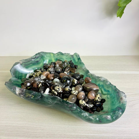 Green fluorite crystal bowl filled with a variety of polished black, white, and brown gemstone tumbles.