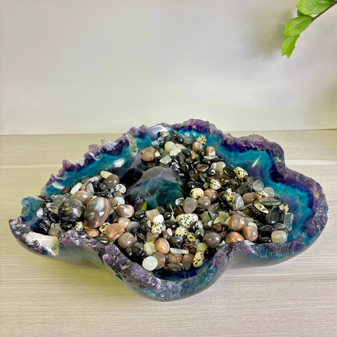 Hand-carved fluorite bowl with raw purple and blue edges, filled with a variety of polished gemstone crystals.