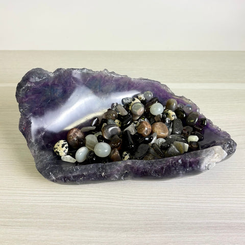 Deep purple fluorite crystal bowl filled with a variety of polished, multi-colored gemstone tumbles and crystals.