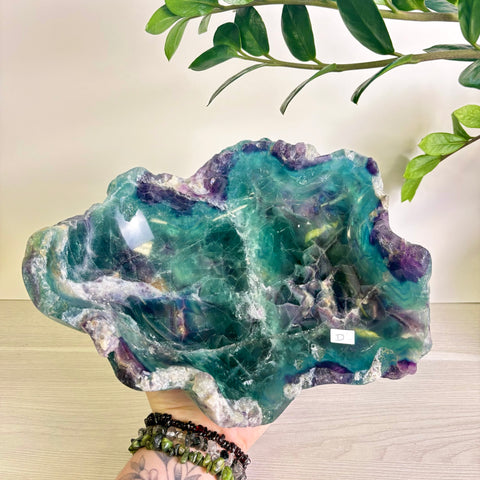 Hand-carved fluorite bowl featuring vibrant teal and purple crystalline patterns with a natural, raw stone edge.