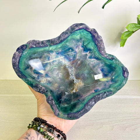 Handheld polished fluorite bowl featuring vibrant swirls of deep purple, teal, and green with a natural raw crystal edge.