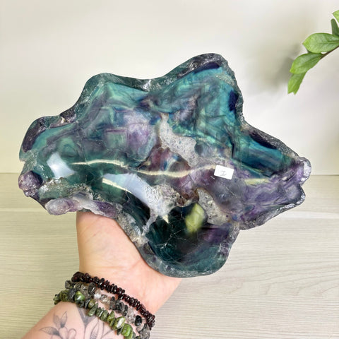 Handheld polished fluorite bowl featuring swirling purple, teal, and green mineral patterns with a natural raw edge.
