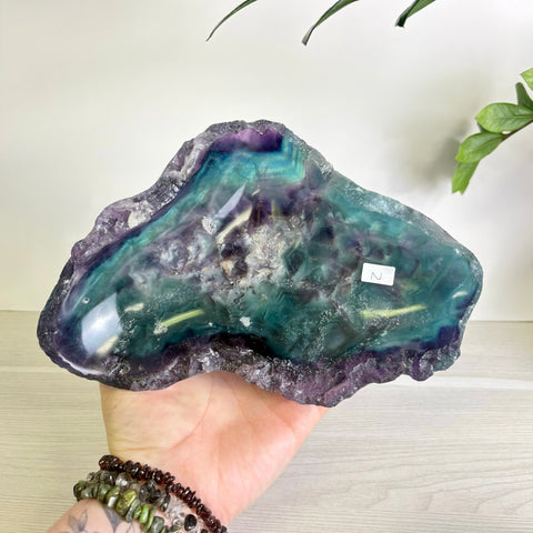 Handheld polished fluorite bowl featuring vibrant swirls of deep purple and teal with a raw, natural crystal edge.