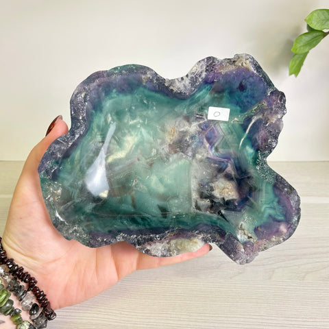 Handheld polished fluorite bowl featuring vibrant swirls of purple and teal with natural crystalline edges.