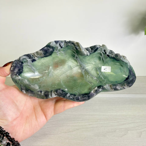 Hand-carved fluorite bowl with natural green and purple crystalline patterns held in a palm.
