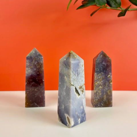 Three polished Nightshade Chalcedony crystal towers with purple, grey, and earthy mineral inclusions on a white surface.