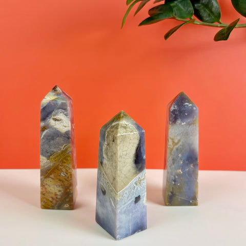 Three Nightshade Chalcedony crystal towers with purple, grey, and earthy yellow patterns against an orange background.