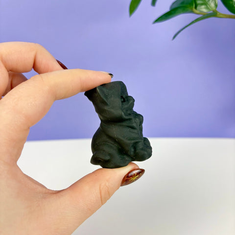Small hand-carved obsidian warlock cat figurine with a hooded cloak held between fingers.