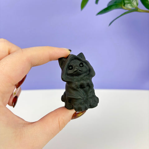Small matte black obsidian warlock cat figurine with a hooded cloak held between fingers.