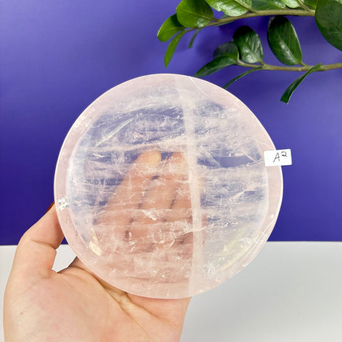 Hand held circular rose quartz crystal plate with natural translucent pink veining and polished finish.