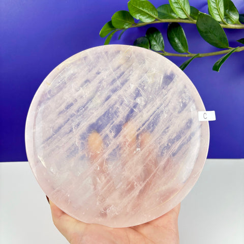 Round, polished rose quartz crystal plate with natural translucent veining held against a blue background.