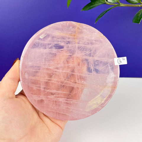 Handheld circular rose quartz plate with natural pink crystalline textures and a polished finish.