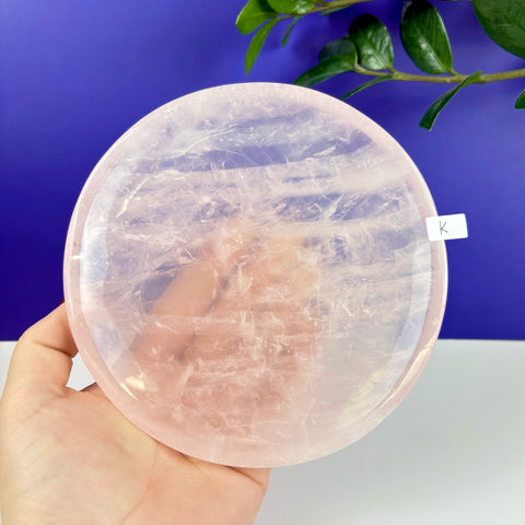 Handheld round plate carved from translucent, pale pink rose quartz with natural crystalline textures.