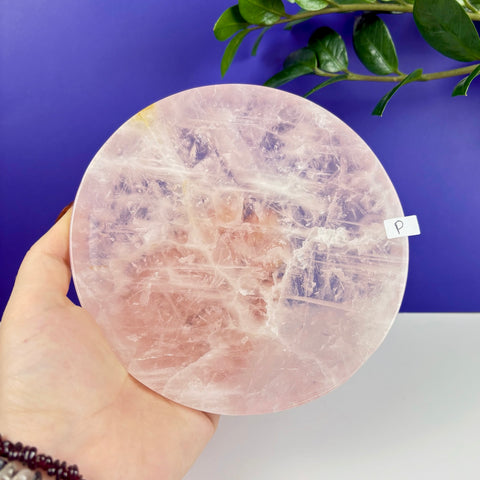 Handheld circular rose quartz plate with natural crystalline textures and translucent pink hues against a blue background.