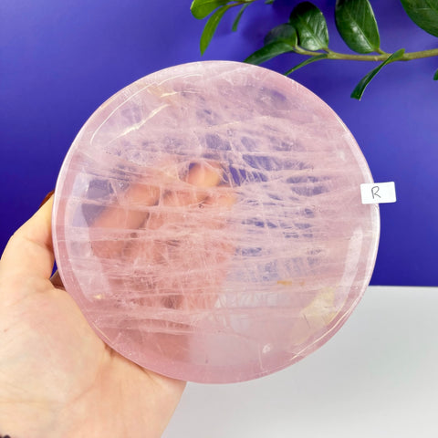 Handheld round rose quartz crystal plate with natural pink veining and a polished finish.