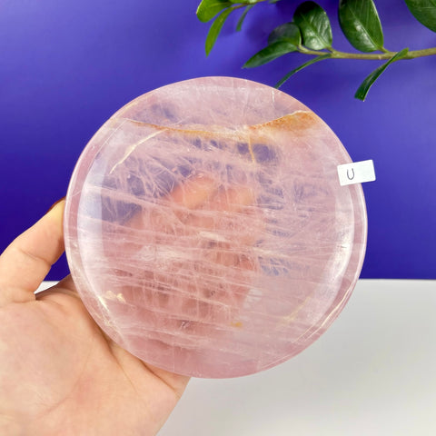 Handheld circular rose quartz plate with natural pink crystalline texture and polished finish.