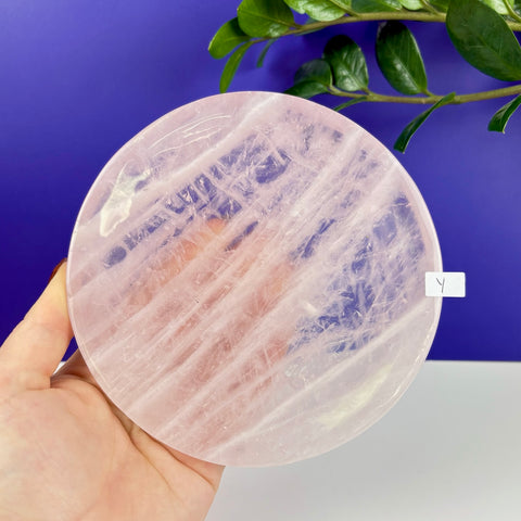 Handheld round plate made of translucent, pale pink rose quartz with natural crystalline textures.
