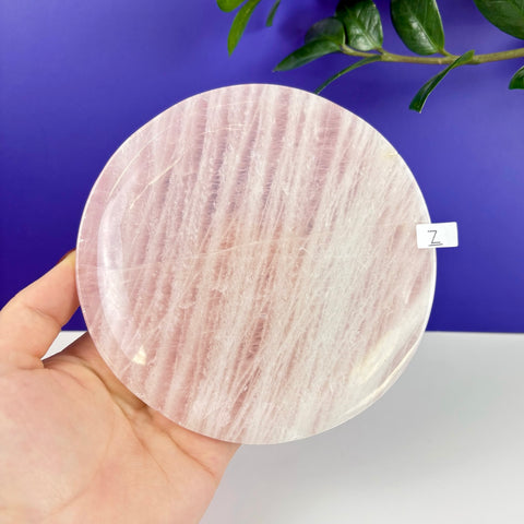 Hand held round rose quartz plate with a polished finish and natural pink striped crystalline texture.